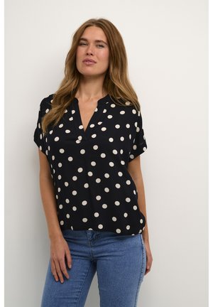 Navy short-sleeve blouse with white polka dots, featuring a collarless design and a loose fit, paired with light blue jeans.