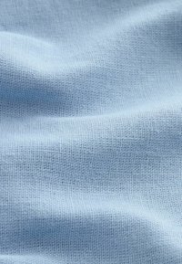 Gros plan d'un tissu tissé bleu clair avec des fils texturés visibles et des plis doux créant des ombres douces.