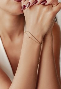 Pulsera de cadena de oro con un diseño sencillo y una pequeña cuenta redonda, llevada en una mano con un tono de piel natural y uñas largas y pulidas.
