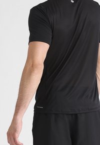 Svart t-shirt med kort ärm för träning, med ett texturerat mönster, en liten logotyp på ryggen nära nacken och en andningsbar design.