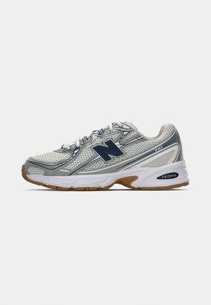 Baskets New Balance 740 blanches et grises avec logo marine, lacets blancs et semelle en gomme, présentées en profil latéral sur un fond uni.