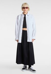 White button-up shirt with red stitching, worn over a black crop top and black maxi skirt. Black sneakers complete the outfit.