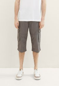Graue Cargo-Shorts im knielangen Stil mit Seitentaschen und glatter Textur. Getragen mit weißen und beigen Sneakern.