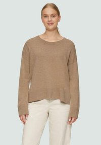 Beige Strickpullover mit einer leicht oversized Passform, weitem Ausschnitt sowie gerippten Bündchen und Saum. Getragen mit hellen Hosen.
