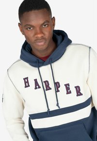 Marineblå og creme hoodie med "HARPER" i røde bogstaver, med snørehætte og en front kangaroo lomme. Blød stofstruktur.