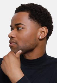 Orecchini tondi in argento indossati da una persona con capelli corti e ricci, vestita con un dolcevita nero, che mostrano una texture liscia e un design minimalista.