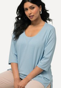 Helles blaues, kurzärmliges Oberteil mit weiter Ausschnittkante und weichem Stoff. Verfügt über eine lockere Passform und seitliche Schlitze für Bewegungsfreiheit.