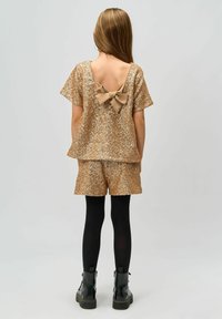 Top dorado con lentejuelas y un detalle de lazo beige en la parte posterior, combinado con pantalones cortos a juego; las medias negras y las botas de tobillo completan el conjunto.