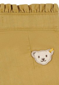 Pantalones cortos caqui con cinturilla fruncida, que presentan un parche de oso de peluche con detalles bordados y un pequeño acento amarillo.
