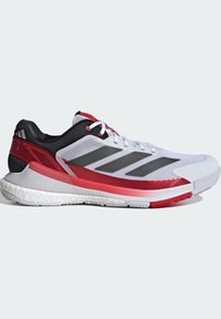 Chaussures de sport avec une tige en mesh blanc, des accents noirs et gris, des détails rouges, et une semelle en caoutchouc texturé pour une meilleure adhérence.