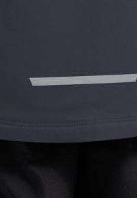 Αθλητικό τοπ σε ναυτικού μπλε χρώμα από λεία ύφανση, με αντανακλαστική οριζόντια λωρίδα στο τελείωμα και ραφές κατά μήκος της άκρης.