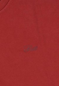 Czerwona bawełniana koszulka z okrągłym dekoltem i subtelnym, haftowanym logo w ciemniejszym odcieniu czerwieni po lewej stronie. Miękka tekstura.