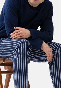 Navy blauwe lange mouwen top met een zak en horizontaal gestreepte pyjamabroek in navy met witte strepen. Zacht katoen, ontspannen pasvorm.