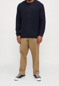 Marinblått stickat tröja med rund halsringning och ribbade muddar, matchat med beigefärgade byxor och svarta sneakers med vita snören och ett mönstrat sula.