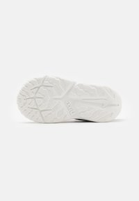 Fehér gumis sneaker talp, amely texturált tread mintázattal, enyhe hullám részletekkel és látható logónyomattal rendelkezik. Tiszta és minimalista dizájn.