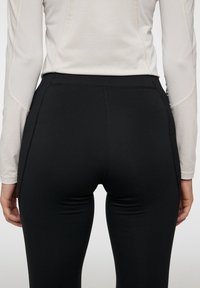 Svarta idrottsleggings med en slät textur, med platta sömmar för komfort. I kombination med en ljus långärmad topp, som har en minimal design.