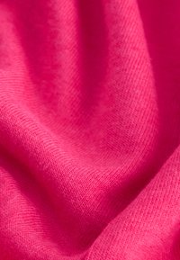 Tissu tricoté rose vif avec une texture visible et des plis doux créant des ombres et des reflets délicats.