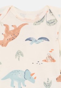 Kortermet body i kremfarget stoff med flerfargede dinosaur- og plante mønstre; inkluderer en triceratops, en pterosaur og en vulkan.