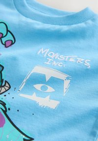 Blå bomulds t-shirt med karaktergrafik, med teksten "Monsters, Inc." og dristige, farverige designs. Glat tekstur og rund hals.