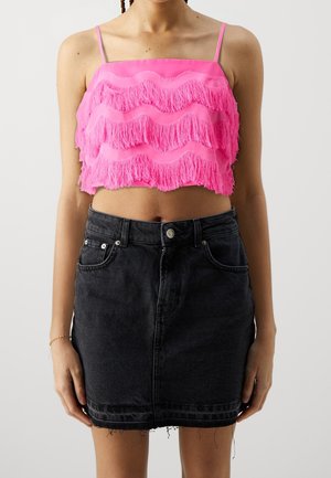 Femme portant un haut court à franges rose vif avec des bretelles fines et une jupe en denim noire taille haute à ourlet effiloché.