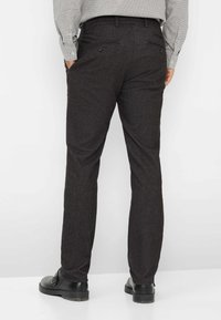 Dunkelgraue maßgeschneiderte Hose aus strukturiertem Material, schlanker, gerader Schnitt und zwei Gesäßtaschen, kombiniert mit schwarzen Schuhen.