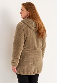Huppari, jossa on pitkähihaiset hihat ja pehmeä taupen värinen fleece, rento malli ja koottu helma alareunassa.