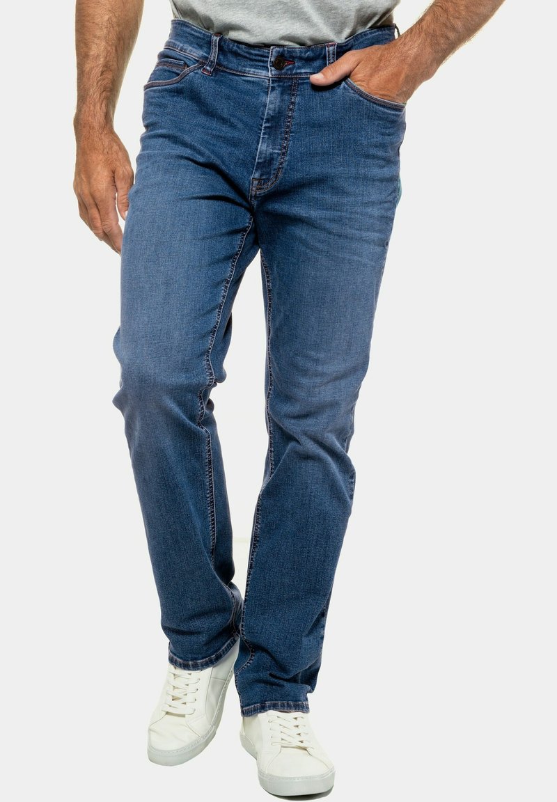 Jeans de mezclilla azul oscuro con corte recto, con costuras de contraste y cierre de botón. Combinados con zapatillas blancas.
