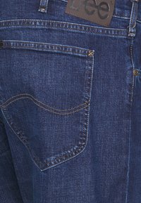 Mörkblå denimjeans med en något texturerad yta, utrustade med en bakficka med kontrasterande sömmar och en märkesläderetikett.