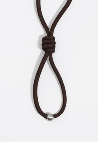 Cordón marrón con una sección anudada y un acento metálico circular plateado. La textura es suave, y el diseño presenta una forma de bucle simple.