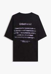 Čierne bavlnené tričko s voľným strihom. Text v purpurovej farbe obsahuje rôzne frázy a na zadnej strane dominuje slovo "Unbothered". Krátke rukávy.