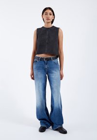 Zwarte cropped mouwloze top met een rafelrand, gecombineerd met blauwe wijde jeans met een geleidelijke vervaging en een design met vijf zakken, geaccentueerd door een zwarte riem.