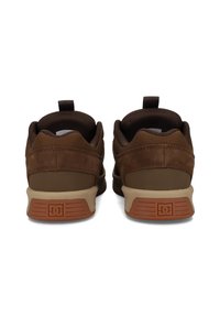 Ruskeakuituiset ja verkkomateriaalista valmistetut urheilukengät, joissa on vaalea kumipohja, kantapäässä vetonauha ja hienovaraisia logo-yksityiskohtia ulkopohjassa.