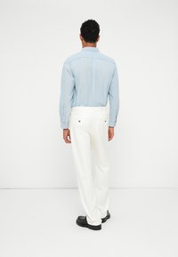 Világoskék, hosszú ujjú ing, fehér, laza nadrág és fekete cipő. Minimalista dizájn, egyszínű anyag, minta nélkül.