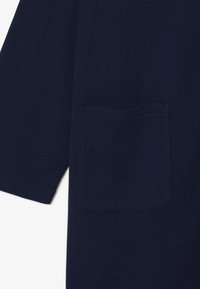 Top in tessuto leggero blu navy con un motivo testurizzato, dotato di una tasca quadrata sul lato sinistro e maniche corte e larghe.
