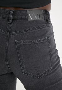 Svarta denimjeans har en slim fit, synlig sömnad och en VMD-logotyp på midjan, med en enda bakficka.