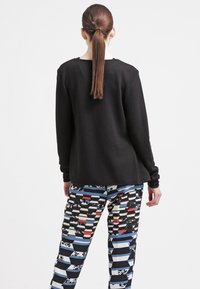Schwarzer strukturierter Pullover kombiniert mit gemusterten Hosen, die Streifen und florale Akzente in Blau, Rot und Weiß aufweisen.