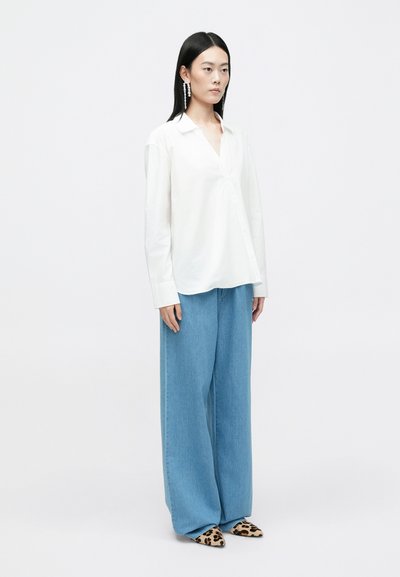 Camisa branca de mangas compridas, tecido leve, ajuste relaxado; combinada com calças largas de ganga azul claro. Footwear apresenta um padrão de leopardo preto e caramelo.