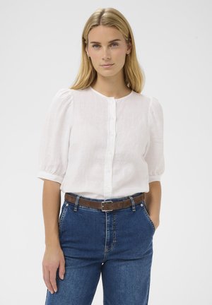 Bela lanena bluza s kratkimi balonastimi rokavi, z gumbi spredaj in okroglim izrezom, kombinirana z modrimi visokim pasom džins hlačami in rjavim pasom.