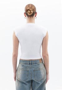 Bílý pruhovaný crop top s krátkým rukávem, kombinovaný s světle modrými džíny s vysokým pasem, které mají zadní kapsy a značkovou etiketu.