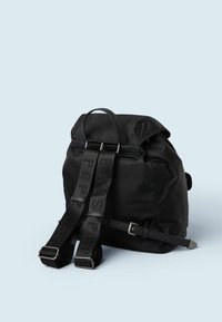 Svart ryggsäck i nylon med ett handtag på toppen, justerbara remmar med logotyp, silverfärgad detaljer och en strukturerad, rundad design.