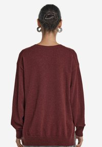 Pull oversize bordeaux en tissu doux et texturé avec un col rond et des poignets et un ourlet côtelés, vu de dos.