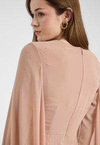Różowa sukienka o eleganckim fasonie, z luźnymi rękawami i ukrytym zamkiem błyskawicznym z tyłu. Gładki, lekki materiał.
