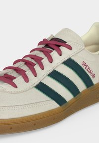 Αντιολισθητικά παπούτσια Adidas Spezial σε εκρού χρώμα με μπορντό κορδόνια, σκουροπράσινες ρίγες, καουτσούκ σόλα και κείμενο "Spezial" στη πλευρά.