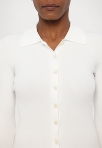 Witte geribde cardigan met een klassieke kraag, voorzien van zes knopen aan de voorkant en een aansluitend ontwerp. Zachte, lichtgewicht textuur.