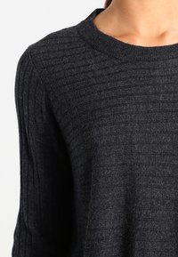 Dunkelgrauer, gerippter Strickpullover mit rundem Ausschnitt, getragen von einer Person, zeigt Oberkörper und Hals.