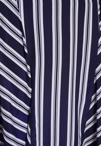 Mřížková modrá tkanina s vertikálními bílými pruhy různých šířek. Hladká, jemná textura s mírným leskem, která obsahuje asymetrický vzor pruhů.