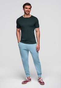Camiseta ajustada de color verde oscuro, pantalones de chándal azul claro con puños acanalados y zapatillas con una mezcla de acentos en burdeos y blanco.