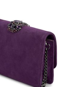 Fioletowa torebka z zamszu z zapięciem zdobionym fioletowymi i czerwonymi kamieniami, połączona z paskiem z czarnego metalu. Gładka tekstura.