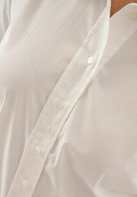 White shirt with a smooth texture, featuring a button placket and soft fabric. Buttons are round and white, with a classic collar.