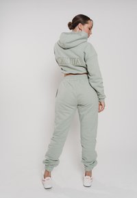 Mintgrüner Crop-Hoodie mit dem eingeprägten Schriftzug "CALUA" auf dem Rücken, kombiniert mit passenden Jogginghosen mit elastischen Bündchen und Taillengummi, getragen mit weißen Sneakers.
